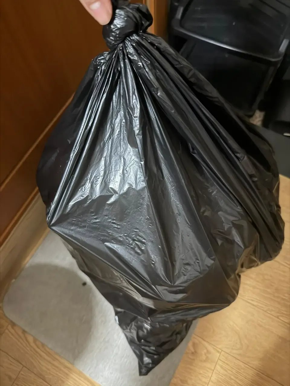 A hand lifting a tied black rubbish bag off the floor