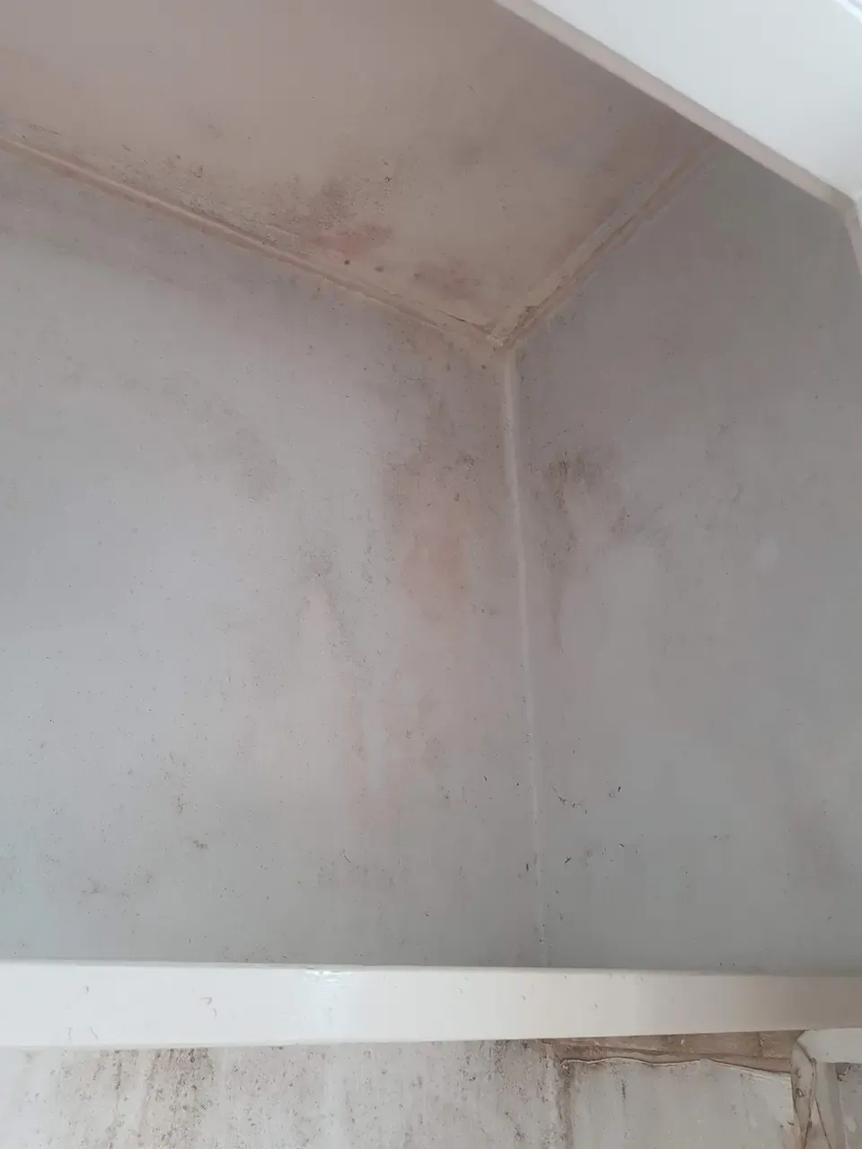 A balcony corner with grey and rust-coloured staining spreading across both walls and along the ceiling joint