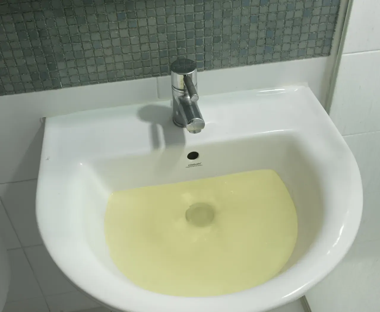 A bathroom basin holding a pool of cloudy yellow water that is not draining