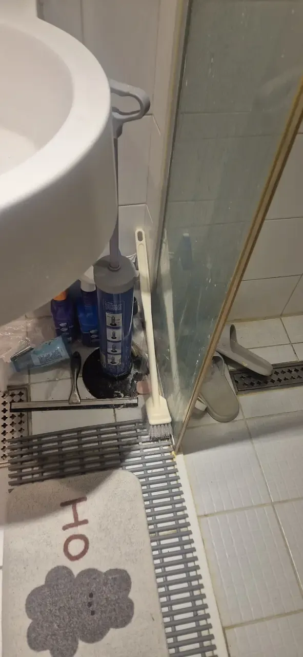 A shower screen before cleaning, the glass clouded with limescale, with a squeegee and drain mat beside it