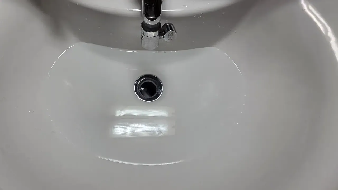 A clean white bathroom basin with a pool of clear water sitting in it that has not drained away