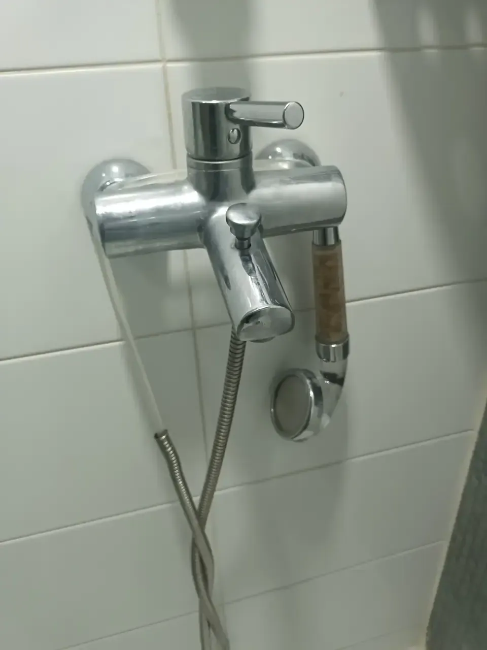 A bath mixer tap with brown limescale and corrosion built up around the shower hose fitting