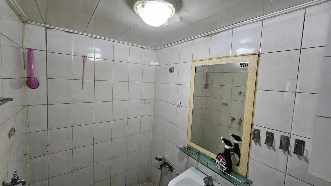 A bathroom at handover with yellowed grout, discoloured sealant and an old framed mirror
