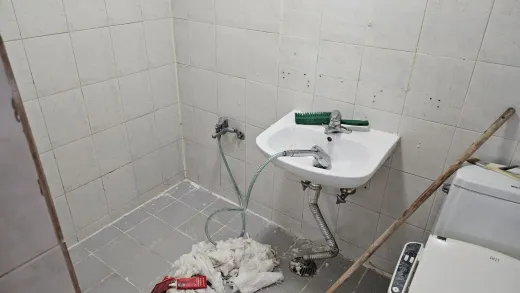 A bathroom during renovation with a newly fitted basin, exposed pipework and a hose on the tiled floor