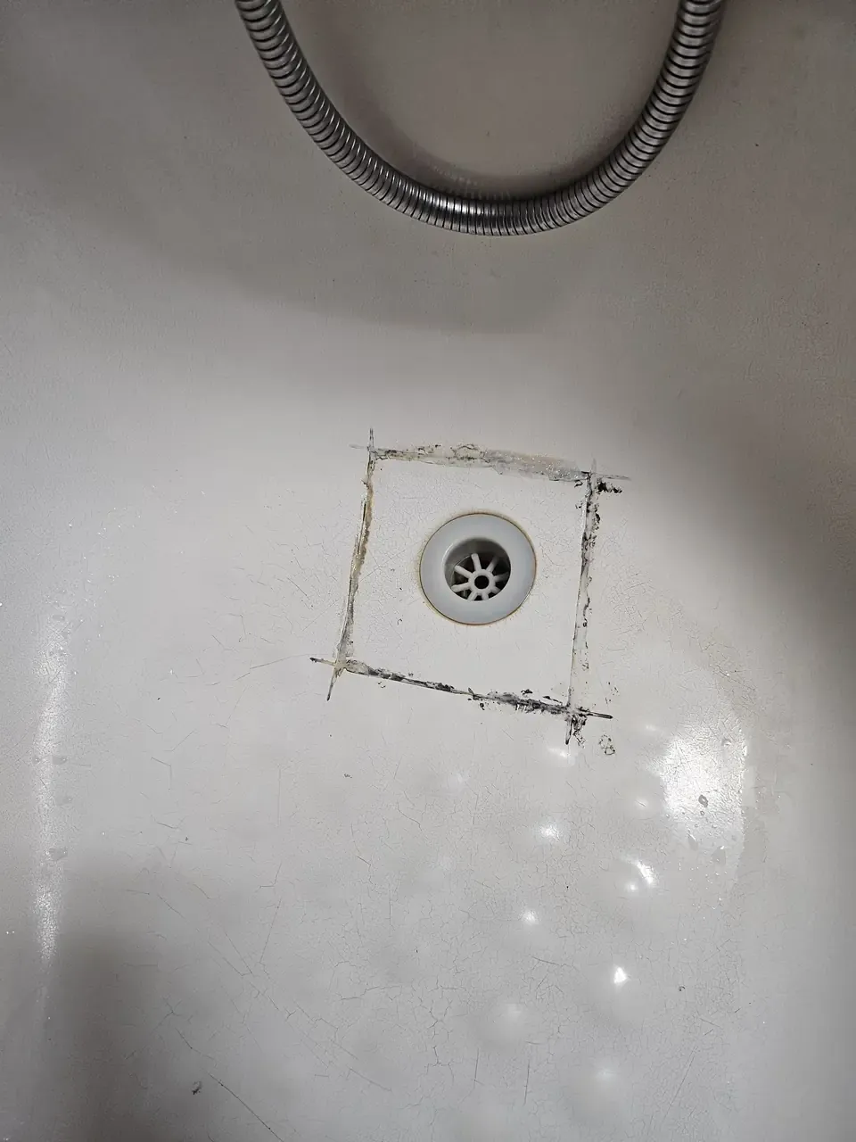 A bathtub where the silicone around the drain has been cut out and replaced by hand, leaving a rough grey square