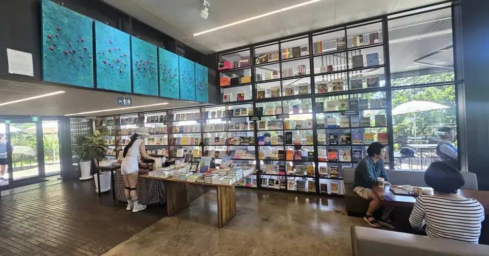 A large bookstore cafe in Seoul with floor-to-ceiling book walls, a central display table and windows looking onto trees