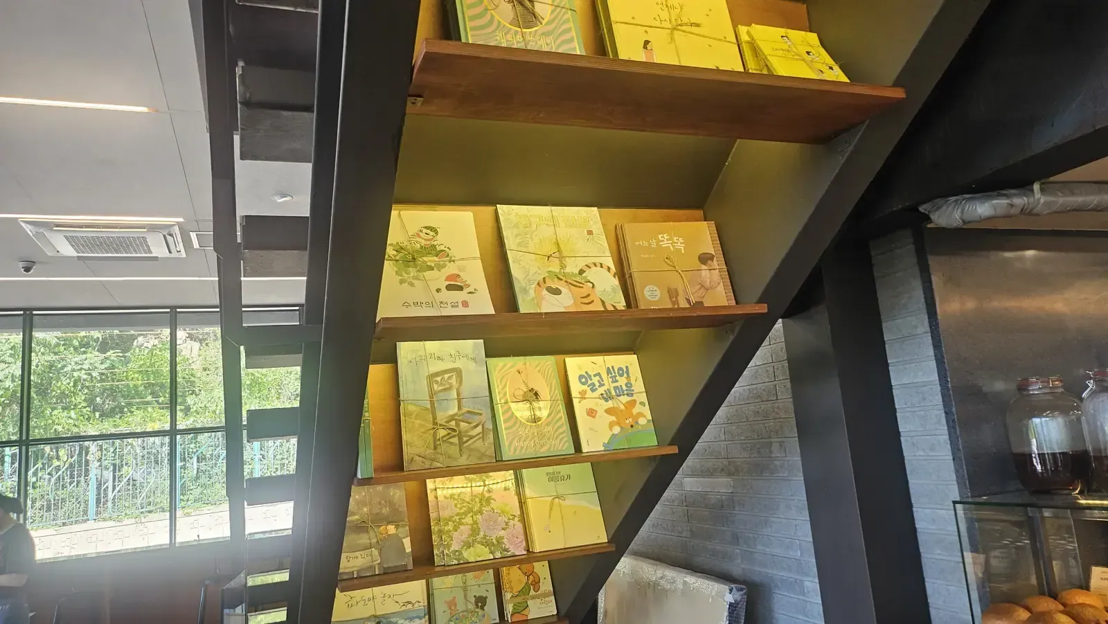 A book display on wooden shelves built into the underside of a staircase in a Seoul book cafe