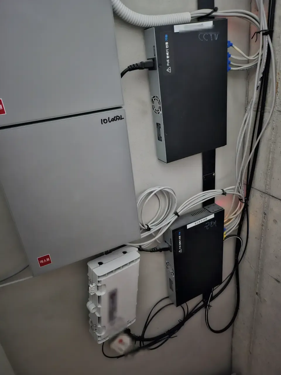 A building's shared communications cabinet with switches, fibre terminals and bundled cabling, identifying labels blurred