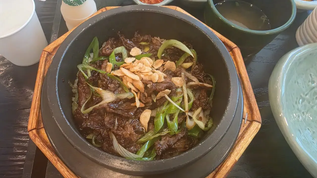 A stone-pot rice dish on a Korean restaurant table with side dishes and water cups