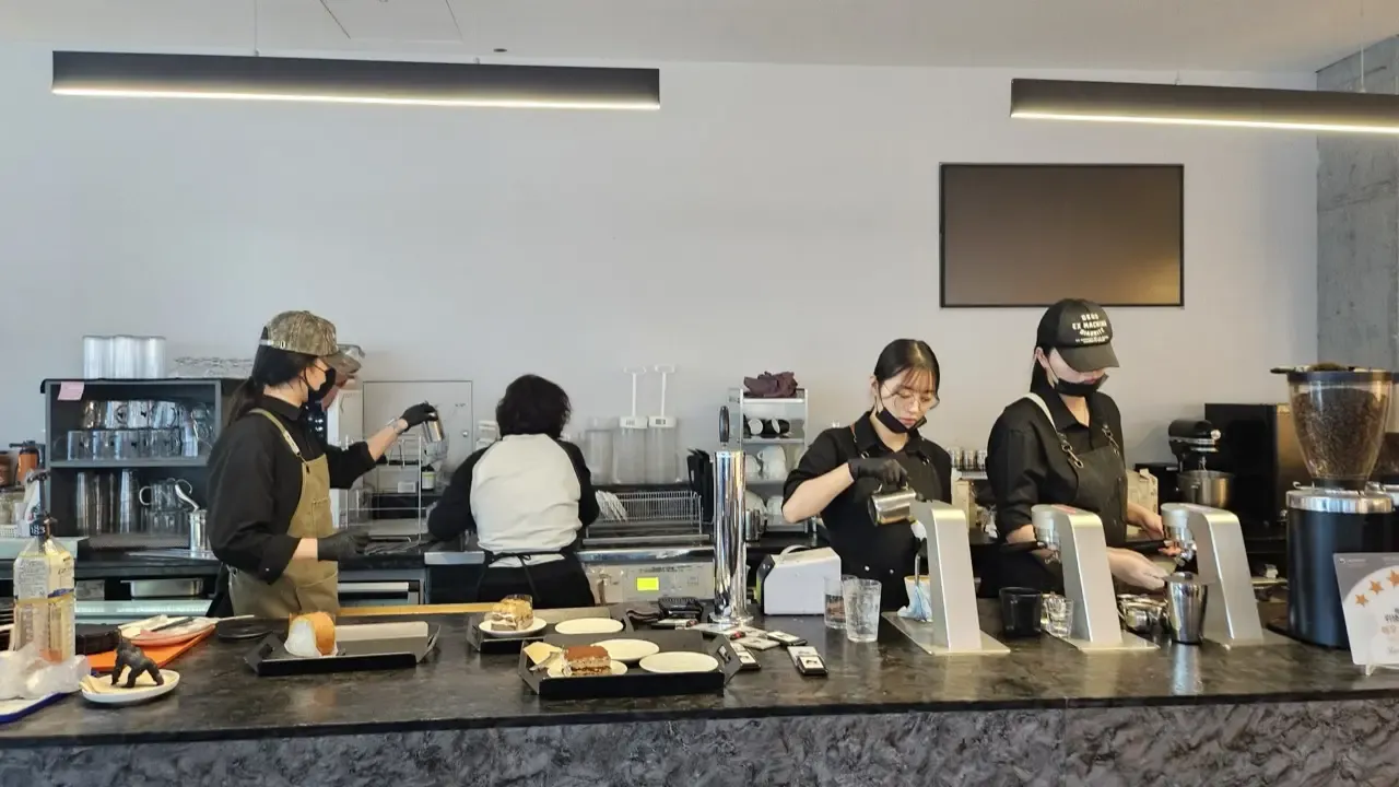 Baristas working behind the counter of a Korean specialty cafe, pouring milk and pulling shots