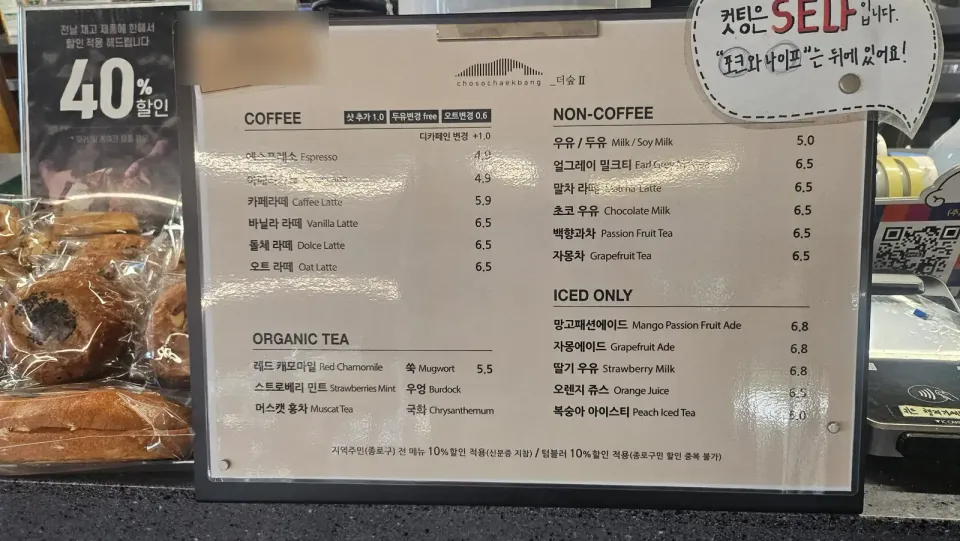 A Seoul cafe counter menu listing drinks in Korean and English side by side, with a handwritten Korean sign taped beside it