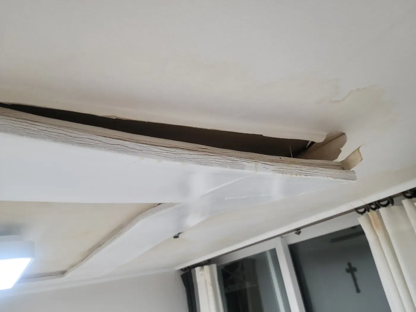 A ceiling cornice detached and hanging away from the wall, with water staining above it