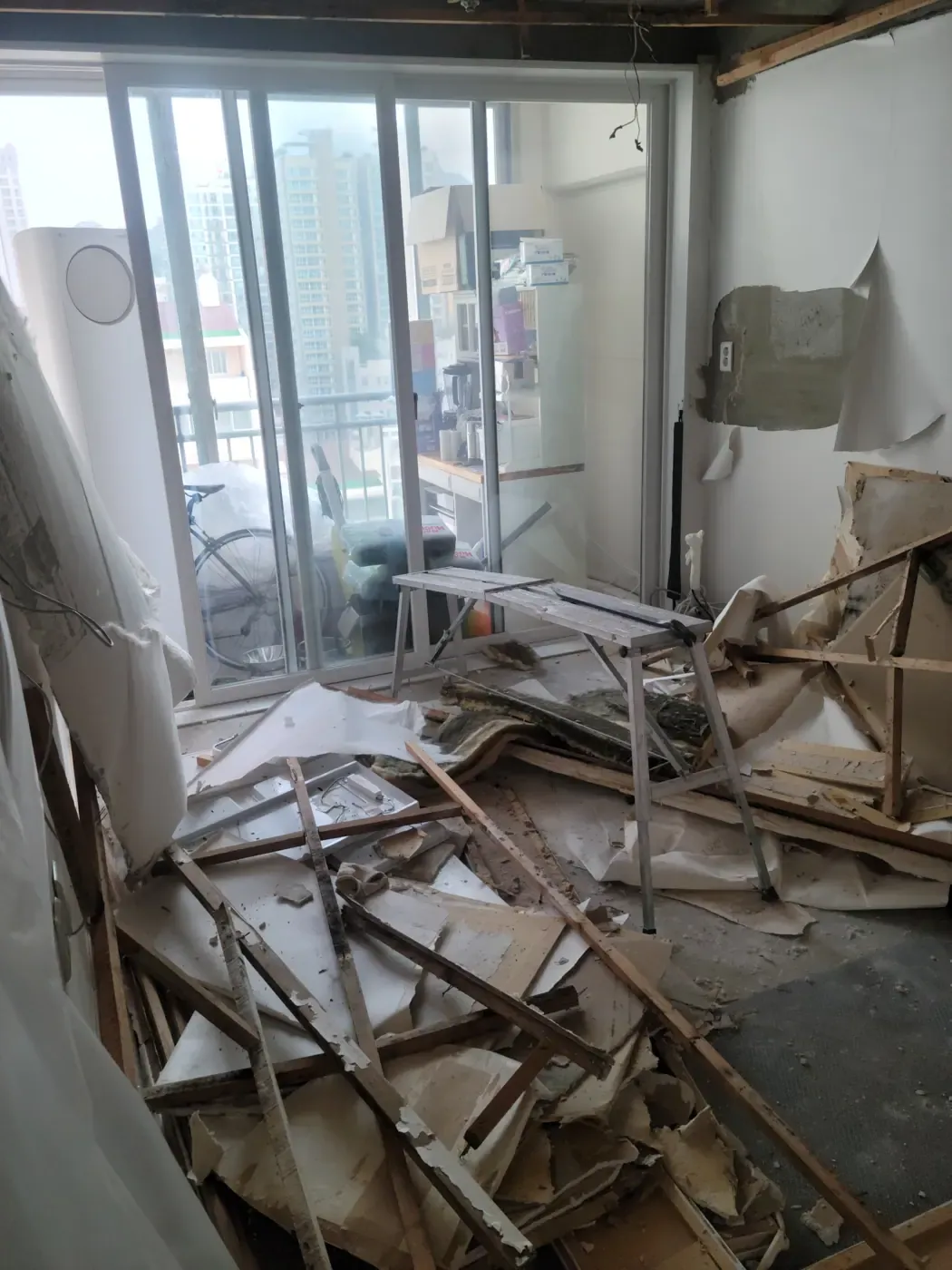 A living room stripped to the concrete slab, ceiling battens and broken plasterboard piled on the floor
