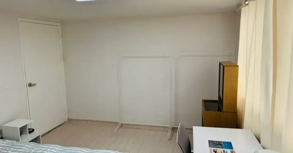 A furnished single room in a Seoul coliving house with a bed, desk and chair beside a curtained window