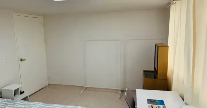 A furnished single room in a Seoul coliving house with a bed, desk and chair beside a curtained window