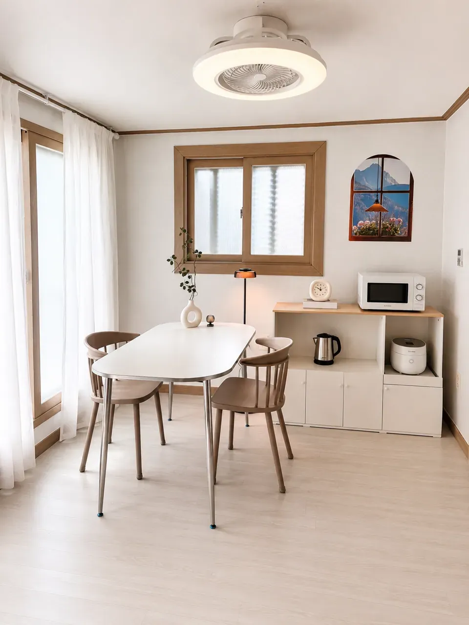 The shared common room: a table and chairs under a ceiling fan light, with a sideboard holding a kettle, rice cooker and microwave