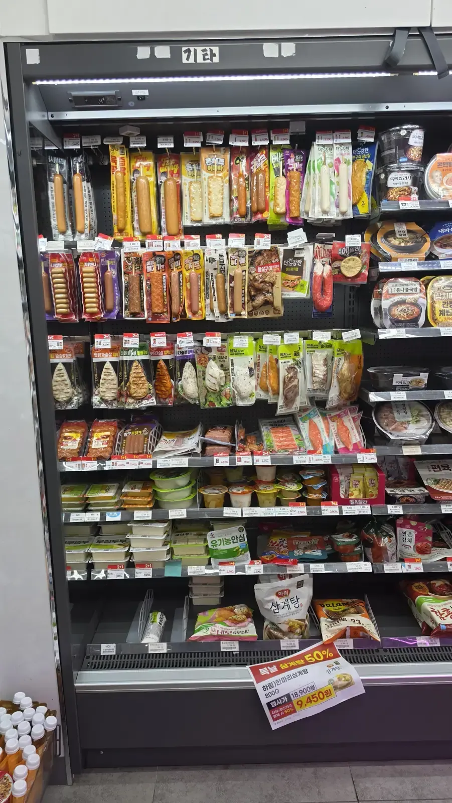 A refrigerated convenience store shelf stacked with sandwiches, rolled gimbap, ready meals and lunchboxes