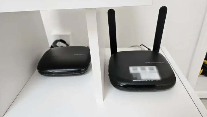 A KT GiGA WiFi home ax router beside its fibre terminal in a cupboard, the credential label deliberately blurred