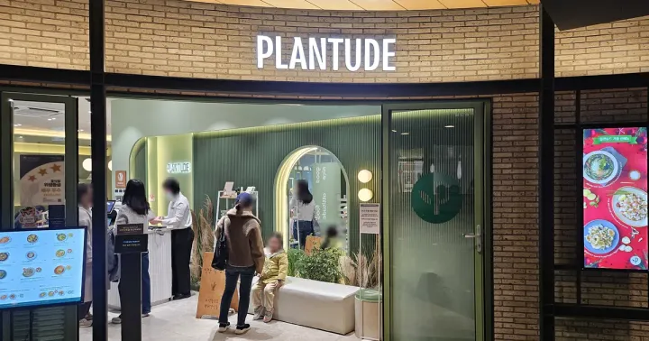 The Plantude storefront at Yongsan I'Park Mall — a lit PLANTUDE sign over a green-walled entrance, with faces blurred