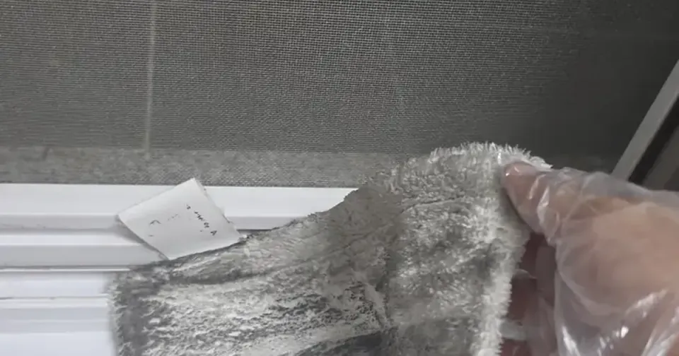A gloved hand drawing a blackened cloth along a white window track
