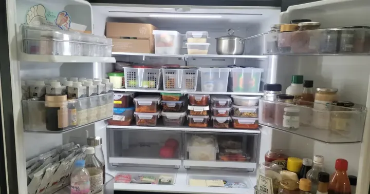 The inside of a Korean fridge after professional organising, with side dishes in matching stacked containers and rows of labelled baskets