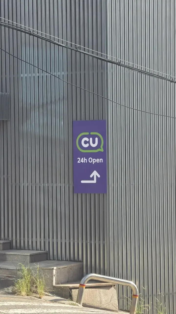 A purple CU convenience store sign reading 24h Open with an arrow pointing around the corner
