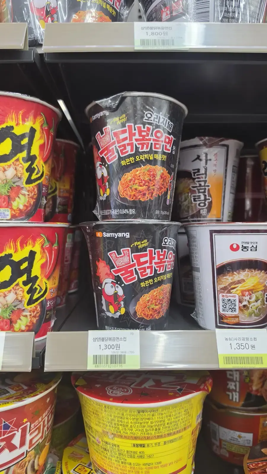 Cup ramyeon on a convenience store shelf with price tags showing 1,300 and 1,350 won