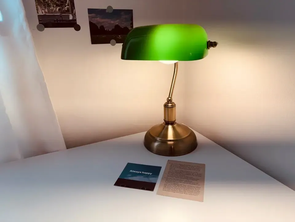 A desk with a green banker's lamp and postcards on the wall