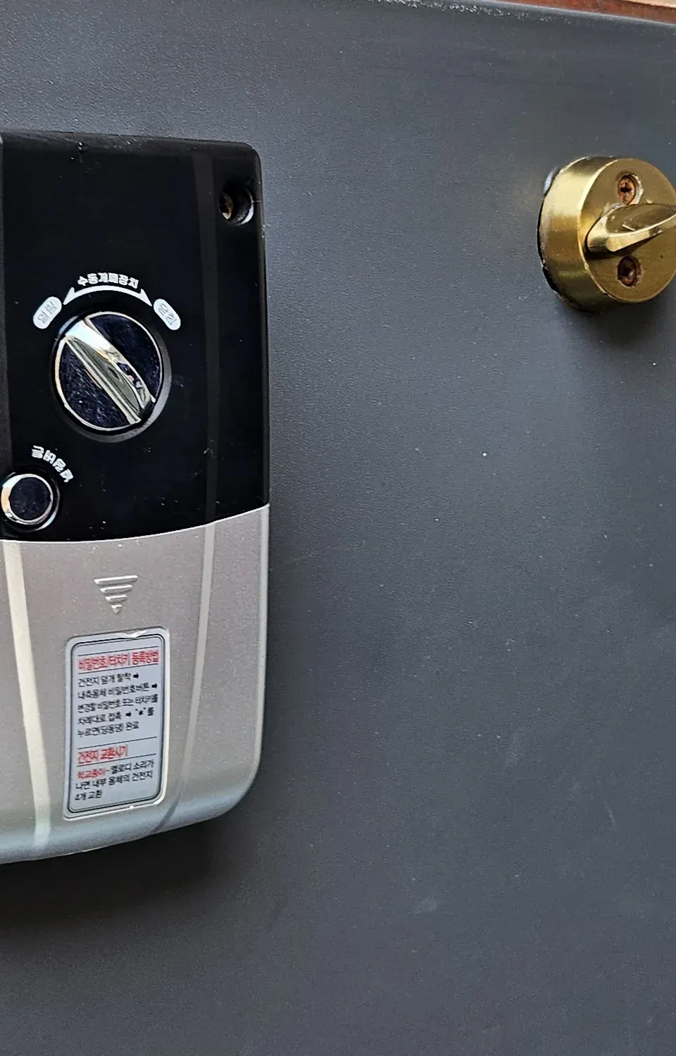 The inside panel of a Milre digital door lock, showing the manual turn knob and a Korean instruction sticker on the battery cover