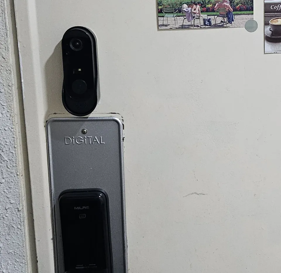 The outside panel of a Milre digital door lock on a Korean flat door, with a video doorbell mounted just above it