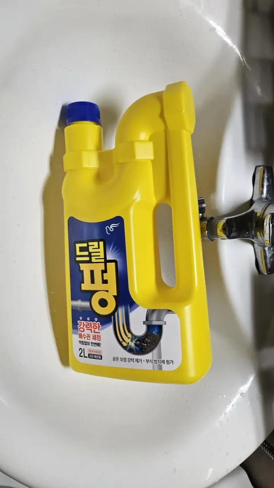 A 2-liter bottle of Korean chemical drain cleaner lying in a white bathroom sink