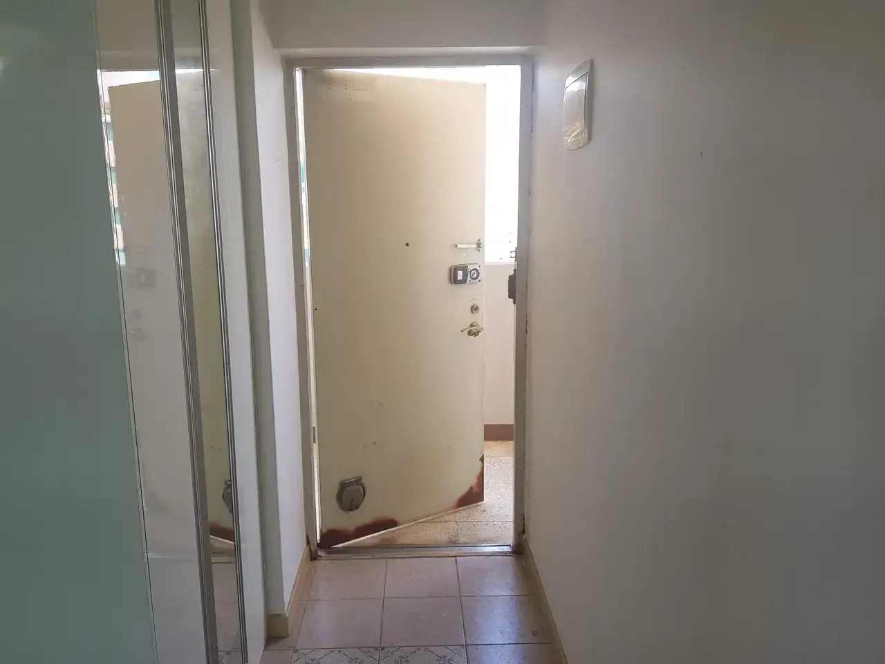 The entrance hall of an empty Korean flat with the front door standing open onto the shared landing