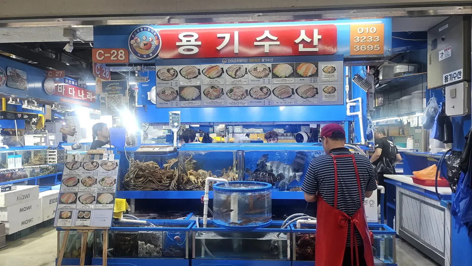 A fish market stall with blue tanks of live fish and crab under a large photo menu board