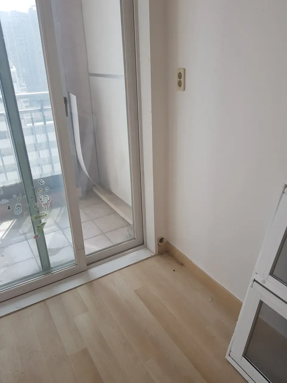 An empty room where wood-effect flooring meets a sliding balcony door, with dust and grit gathered along the skirting and the door track