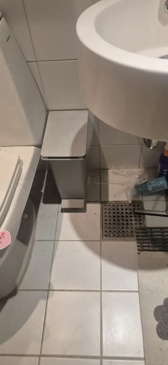 Bathroom floor beside a basin before cleaning, hair and grime collected along the grout lines and around the floor drain
