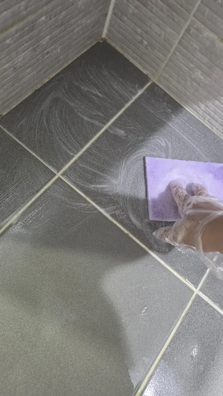 Bathroom floor tiles covered in foam with a gloved hand scrubbing