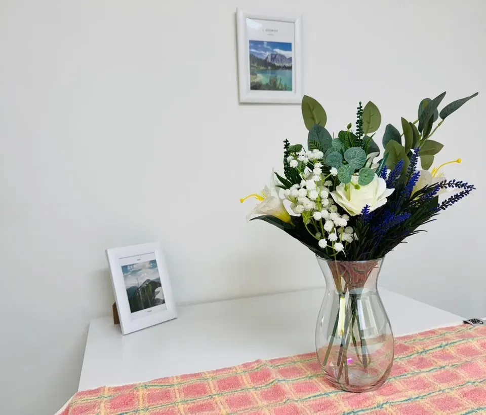 A vase of flowers on a white desk beside a framed photograph
