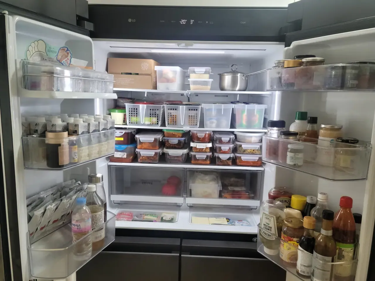 The inside of a Korean fridge after organising, side dishes in matching stacked containers with rows of labelled baskets above