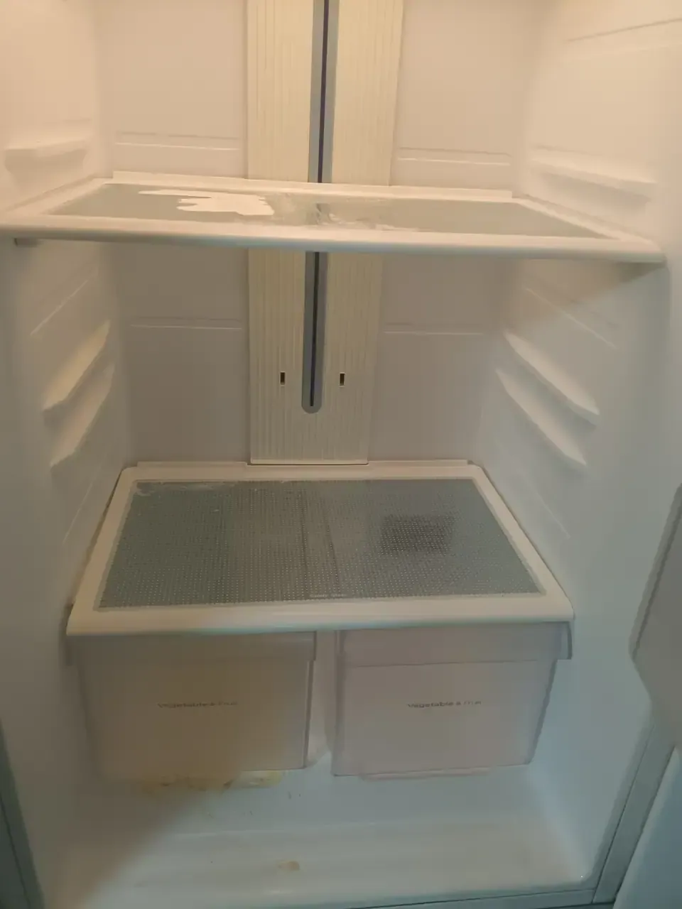 The inside of a fridge with empty shelves and dried spills in the base