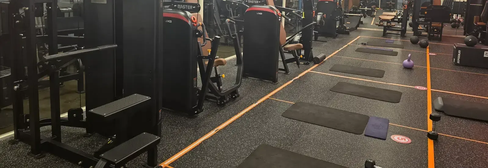 A row of weight machines beside a matted training floor marked out with orange lines at a Seoul gym