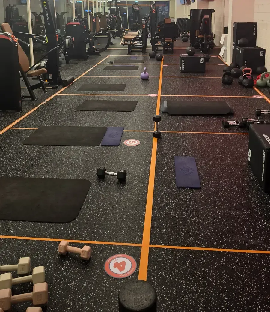 A matted gym zone with numbered floor markers, kettlebells, dumbbells and plyo boxes