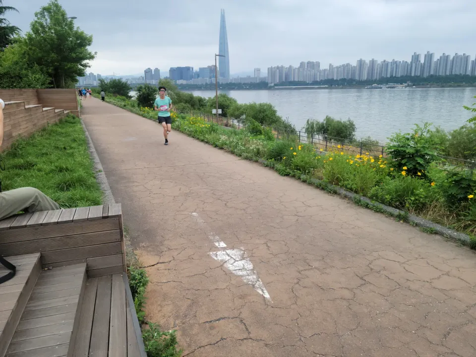 A runner on a paved path beside the Han River in Seoul, with the Lotte World Tower and apartment blocks across the water