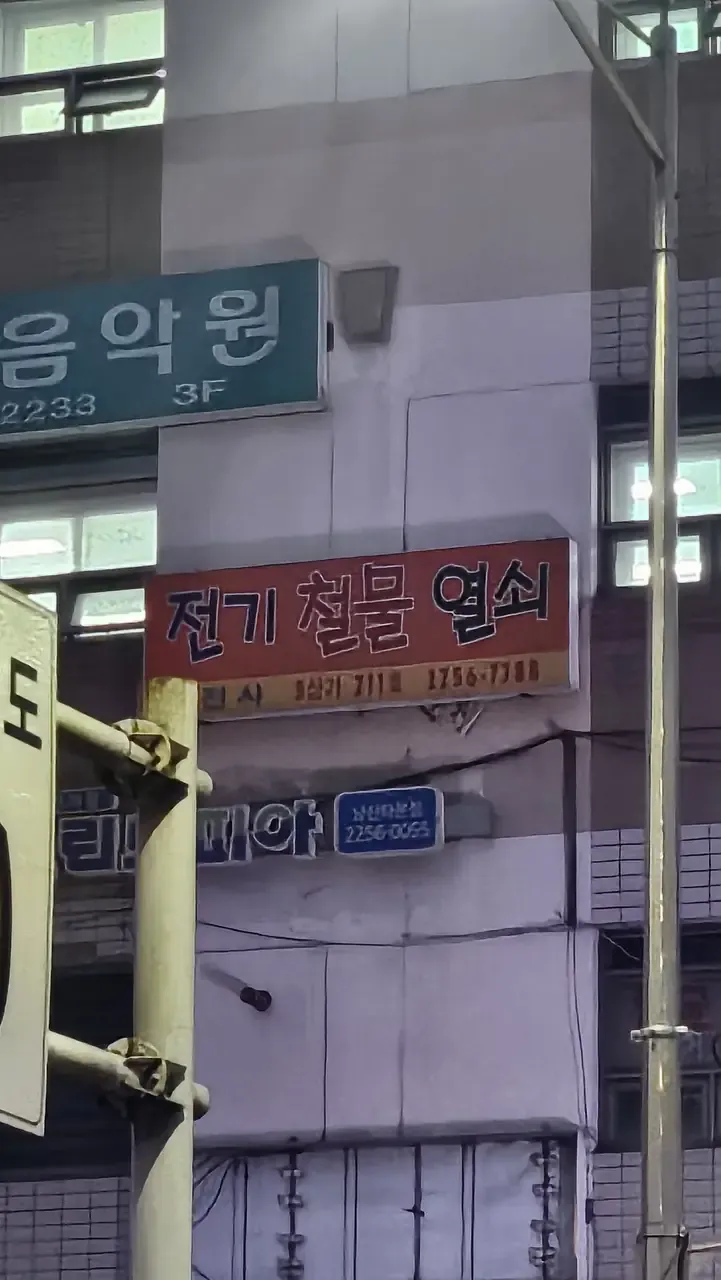 A shop sign high on a Seoul building reading 전기 철물 열쇠 — electrical, hardware, keys