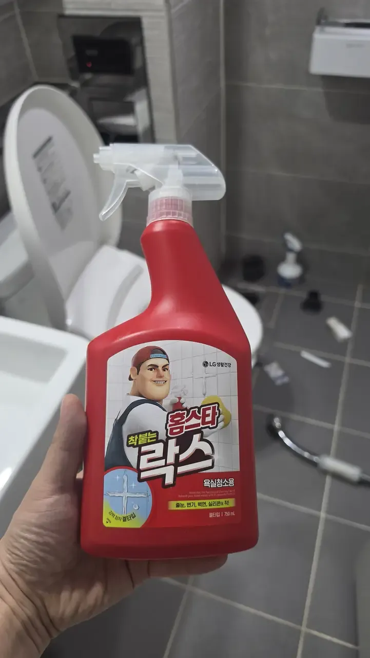 A bathroom cleaning spray bottle held up in a Korean bathroom mid-clean