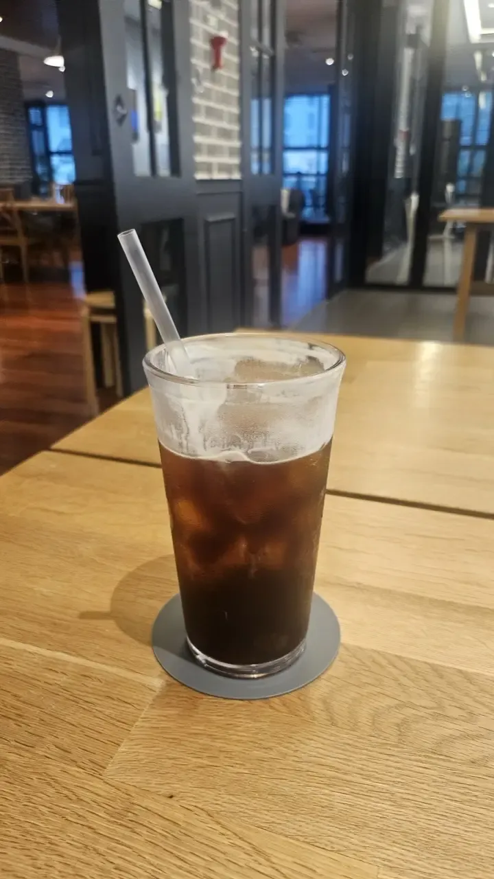 An iced americano on a large wooden table in a spacious Korean cafe with empty seats around