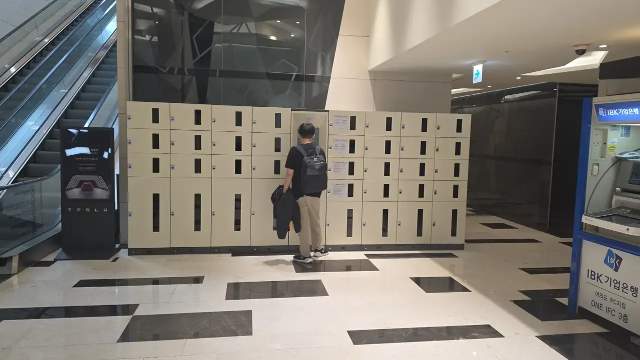 Rows of beige lockers in IFC Mall beside an IBK bank ATM, with a shopper at the payment screen