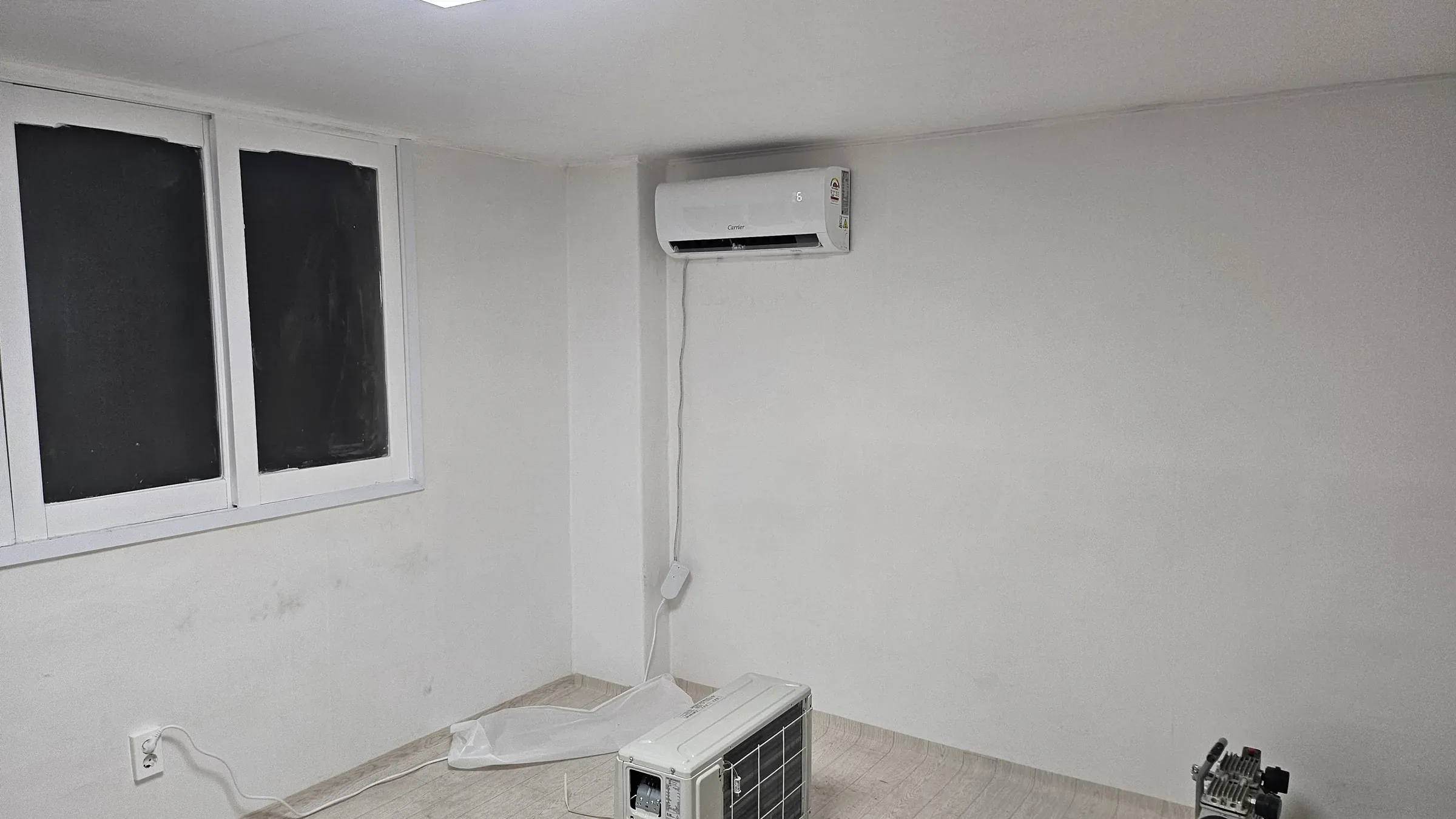A wall air conditioner mounted on a wall with its matching outdoor unit still standing on the floor below, waiting to be installed
