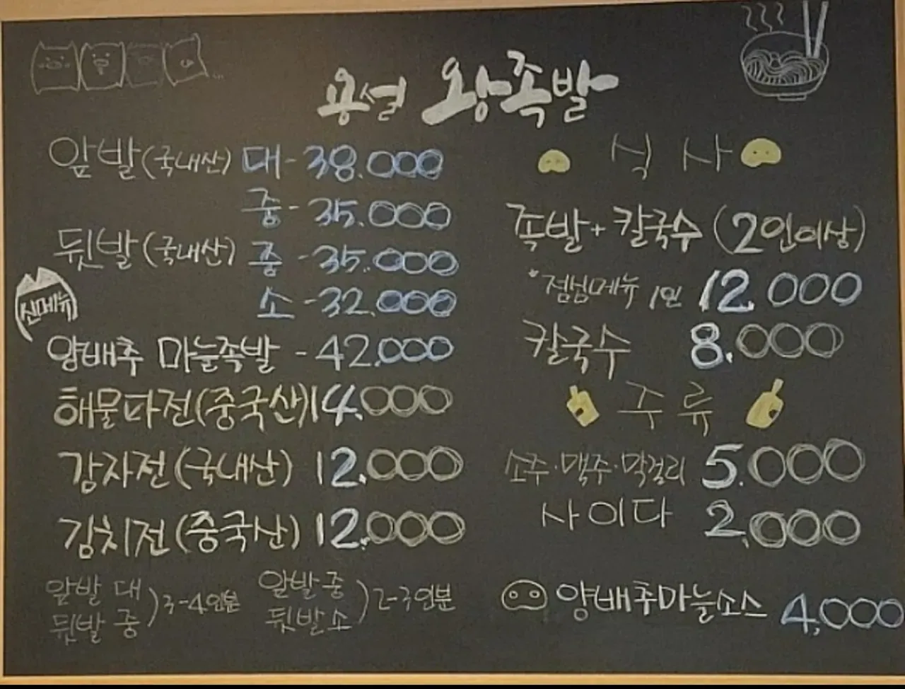 A handwritten chalkboard menu at a Korean pork-trotter restaurant, with the origin of each dish written in brackets — front and rear trotters marked Korean, potato pancake Korean, seafood pancake and kimchi pancake marked Chinese