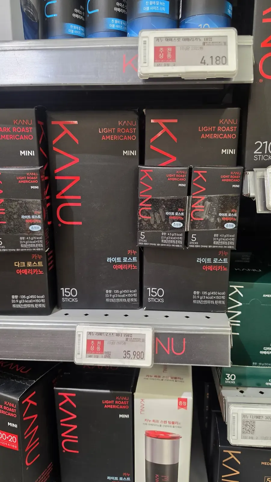 Boxes of KANU Light Roast and Dark Roast Americano mini sticks on a shelf, including five-stick boxes, with a price label reading 35,980 won