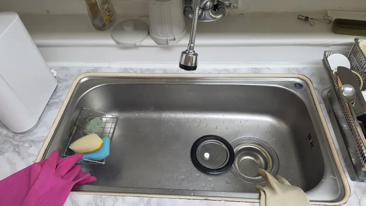 Gloved hands scrubbing a Korean kitchen sink, strainer baskets out
